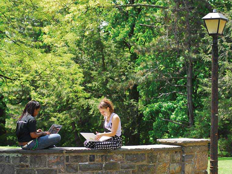 Exterior, two students sitting on low wall