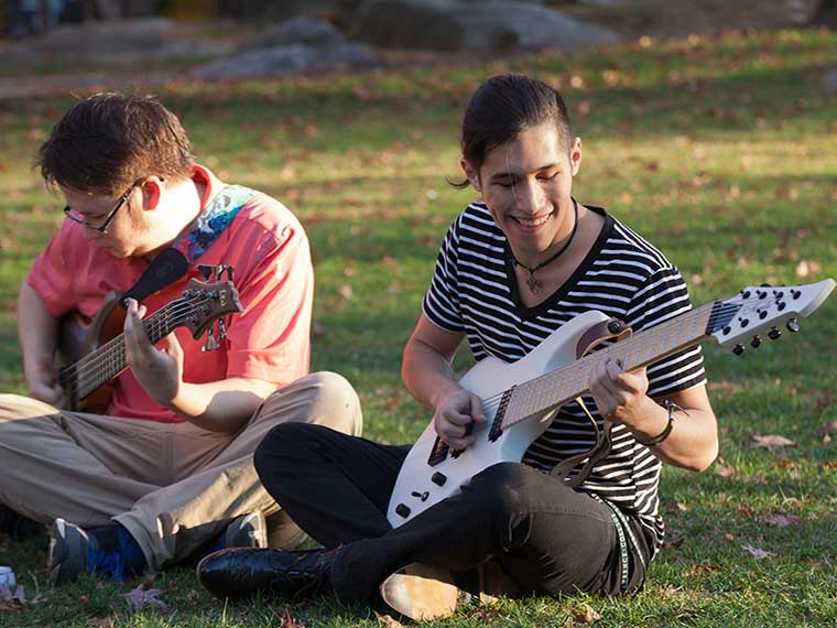 Students seated on grass playing guitar
