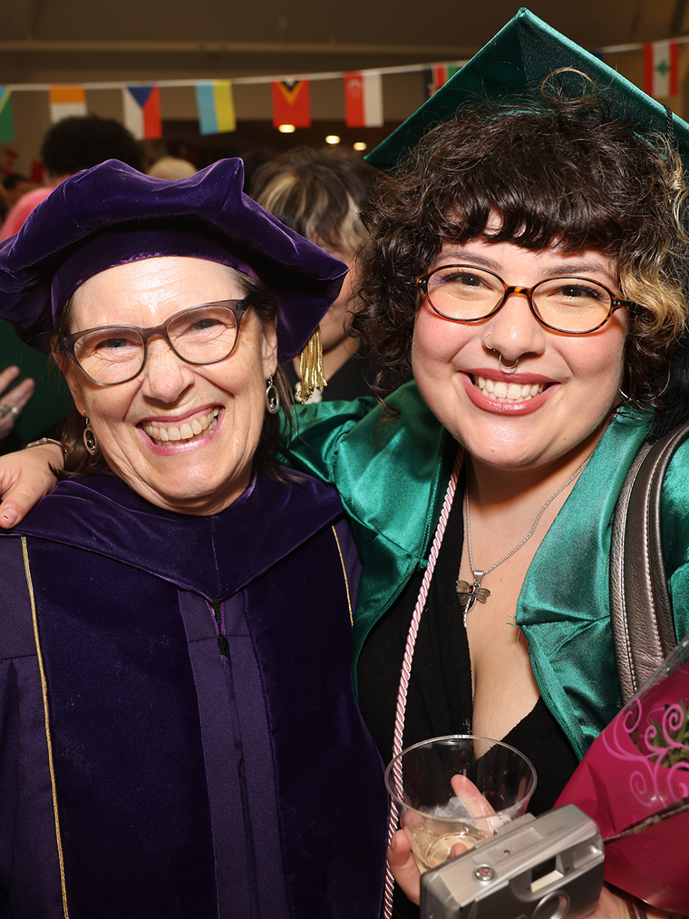 Faculty member and student embrace in commencement regalia