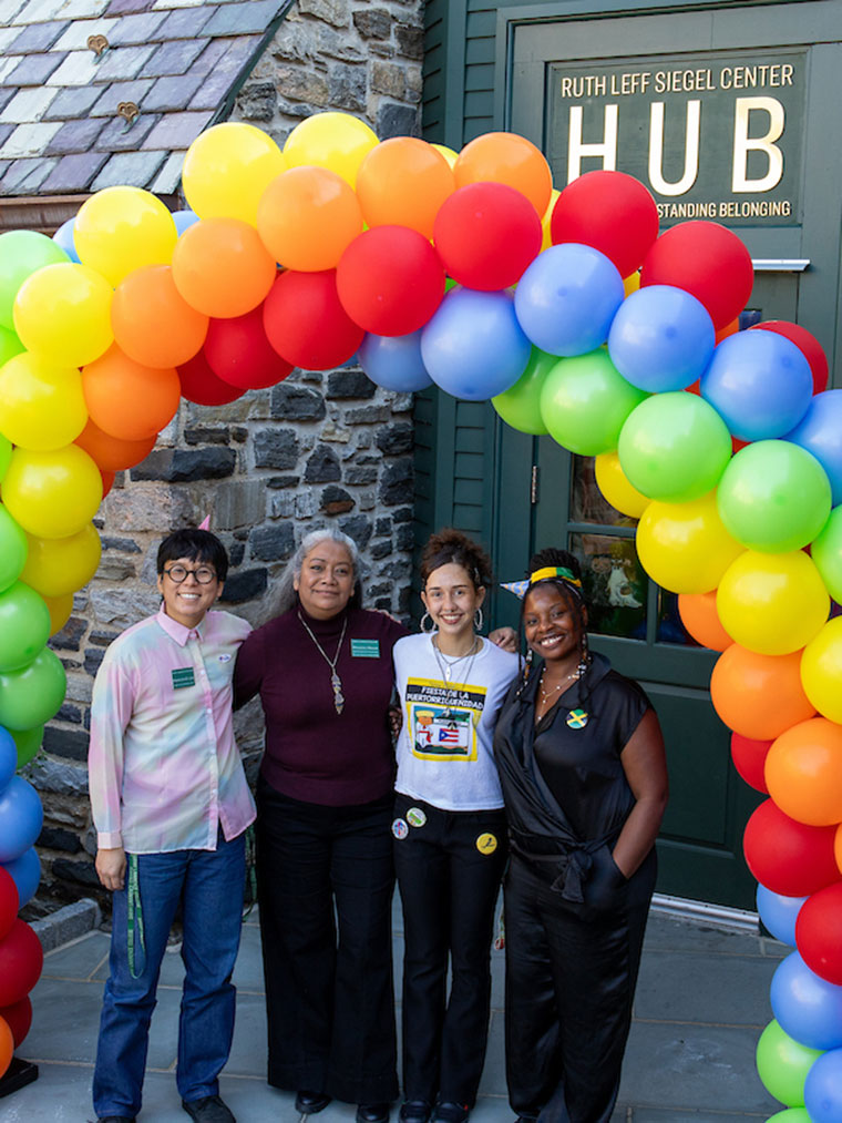Four people standing under a colorful balloon arch in front of a building named The HUB