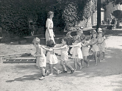 A teacher and students play follow the leader in the 1930s