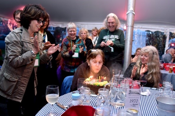 Picture of person blowing out candles on birthday cake surrounded by people clapping