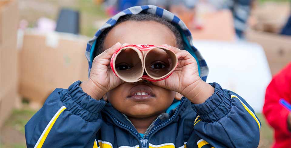 small child holding cardboard tubes as binoculars
