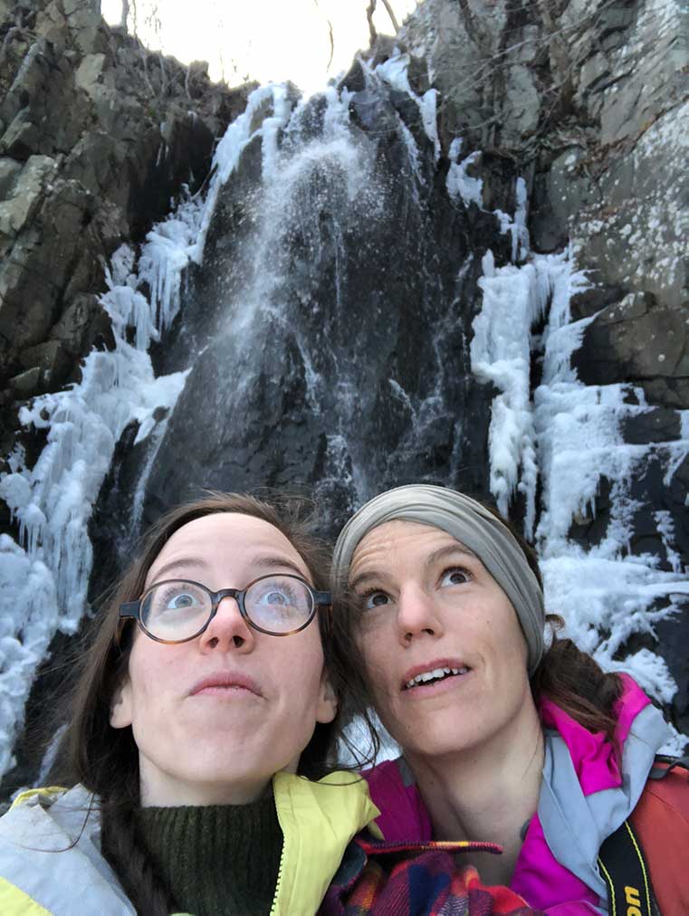 Selfie-style photo of Emily and Tanya with high waterfall behind them