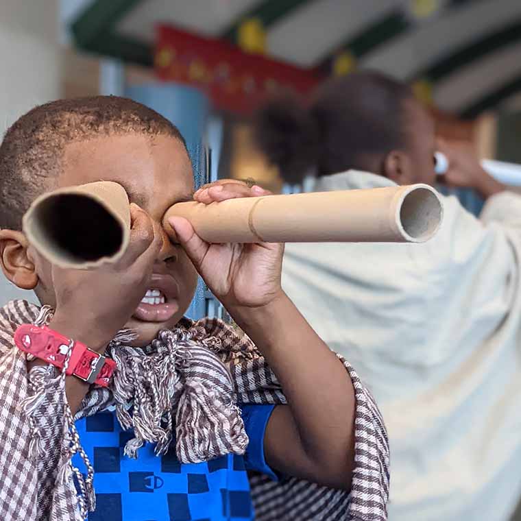 Little boy holding cardboard tubes to his eyes like telescopes