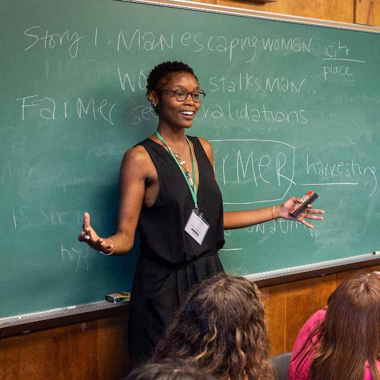 Writing teacher gesturing with arms wide and smiling at class