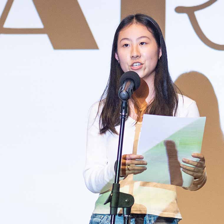 Student speaking on stage in front of a large projected word cabaret