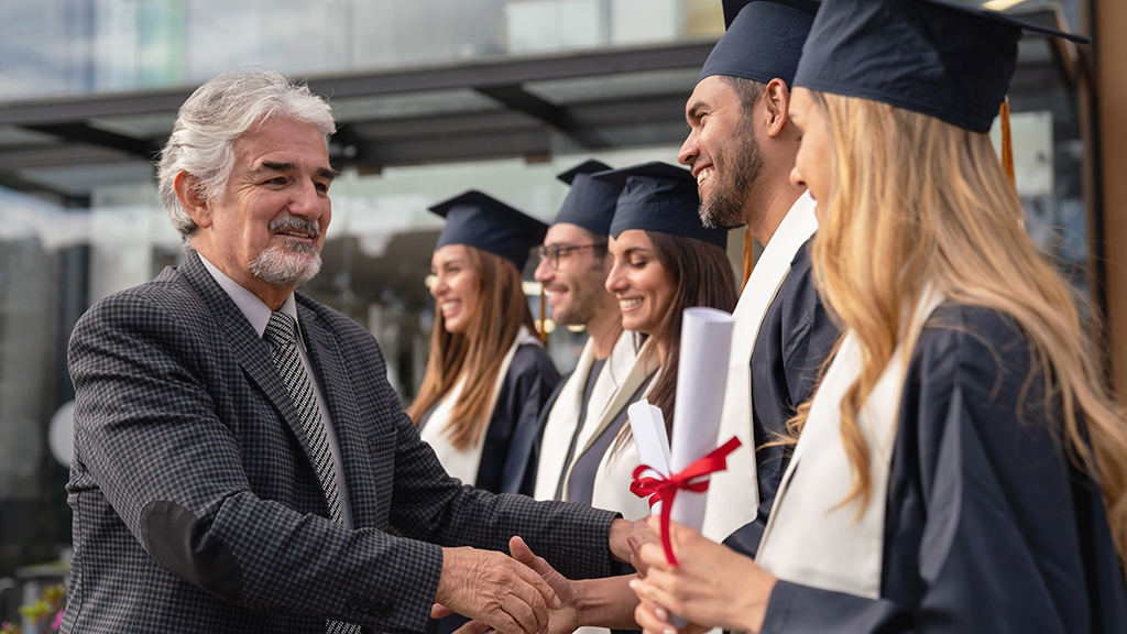 A man shaking hands with graduates in cap and gown
