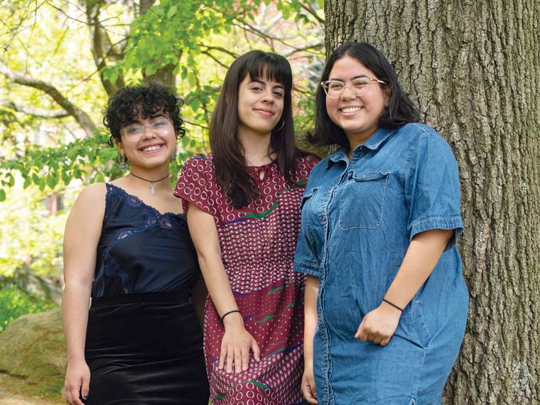 Photo o three people standing together outside near a tree.