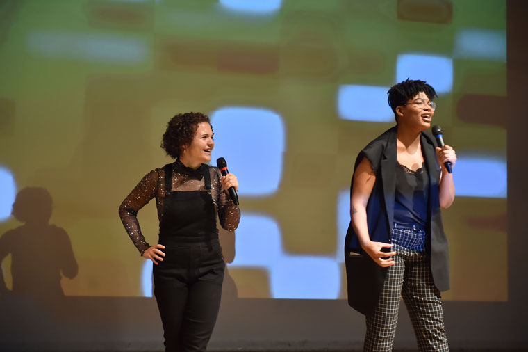 Two people on stage in front of a projected mosaic pattern