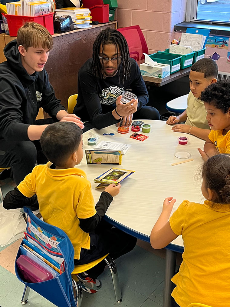 Two basketball players engage with students around a table