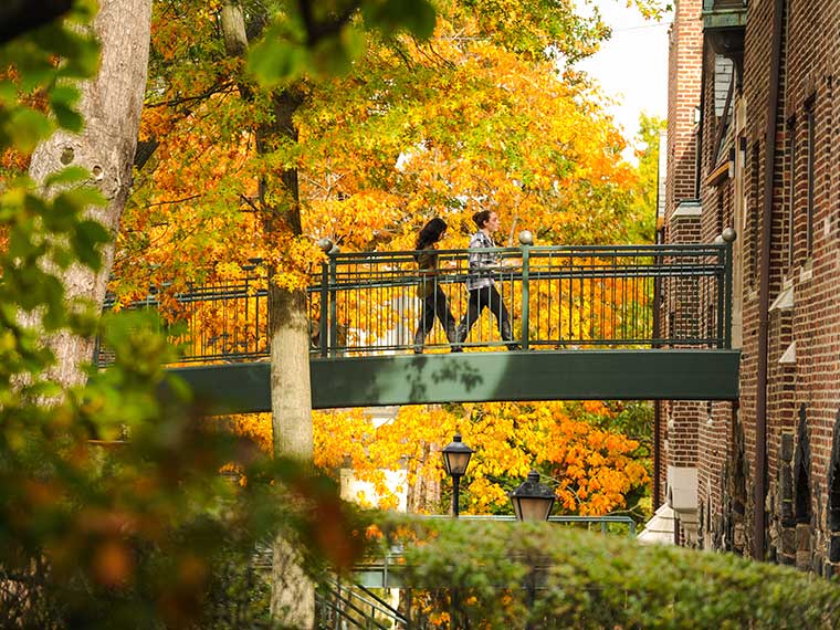 Fall foliage, two student walking over footbridge