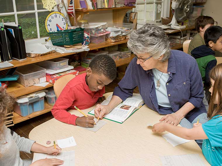 pre-school teacher working with three students on writing