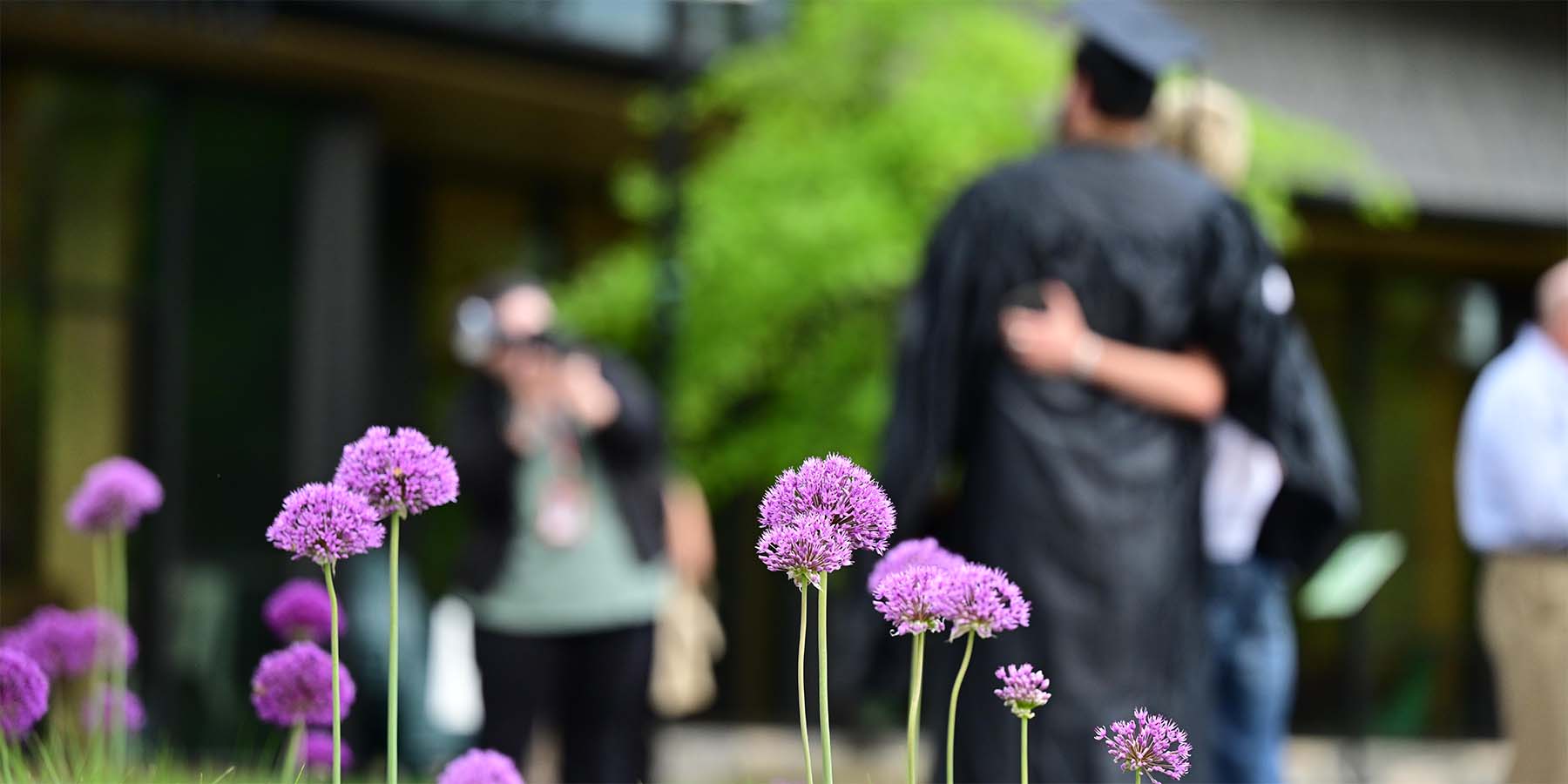 purple flowers in foreground; graduate with family in background