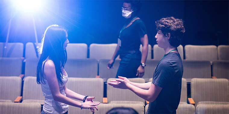 two students facing each other with hands extended, backlit by a project