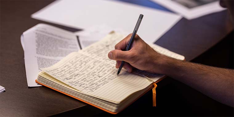 closeup of hand holding pen and writing in journal