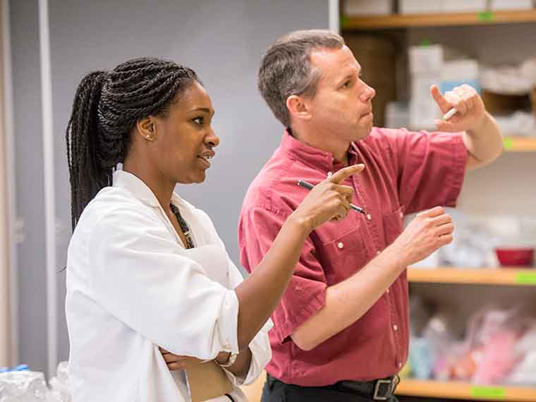 Student in lab coat standing with chemistry faculty member