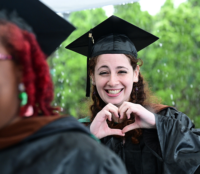 Graduate making a heart sign with their hand in the rain
