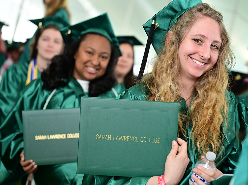 Students in caps and gowns smiling and holding diplomas