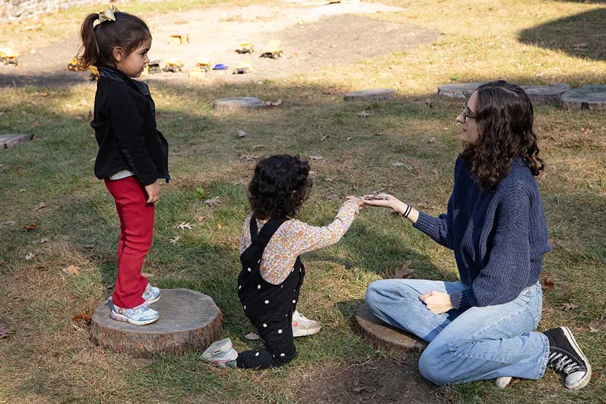 Young girls playing with college student teacher in play yard.