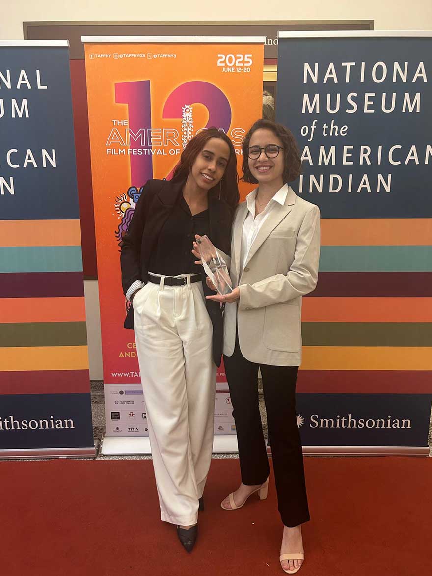 Two women in front of film festival background. Woman on the right holds a crystal award.