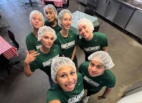 Women's soccer team members pose for selfie in community kitchen.