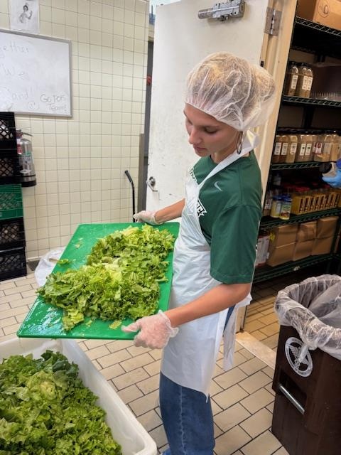 Women preparing lettuce for salad in community kitchen.