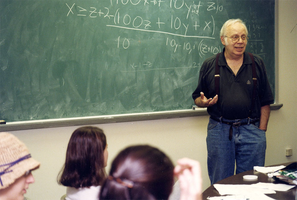 Joseph Woolfson in front of a blackboard speaking to a class