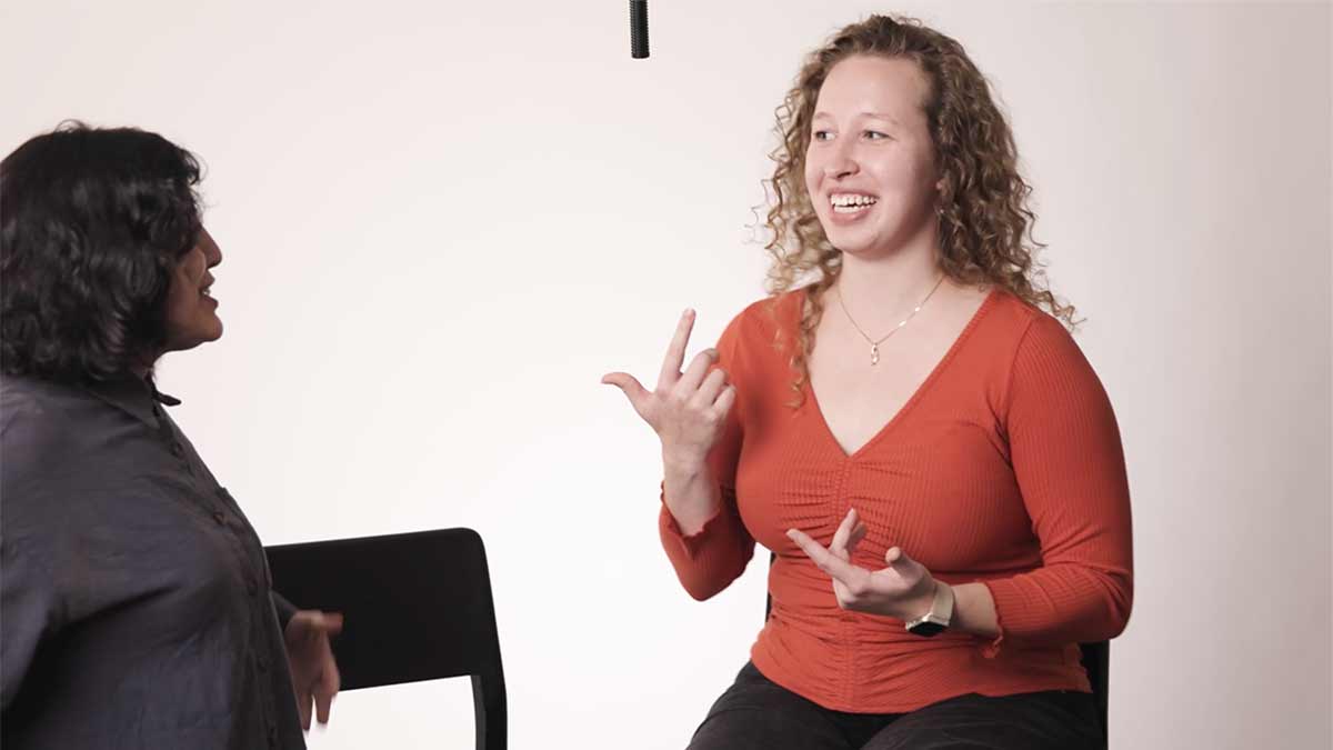 two people talking indoors. One standing one sitting. 