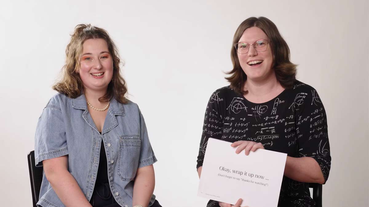 two women sitting looking at the camera. One holding a white paper.