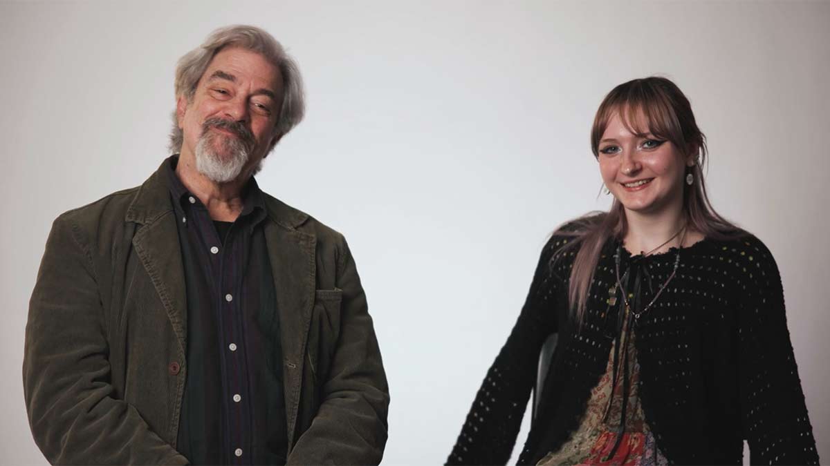 A man and woman seated smiling at the camera against a plain studio background.
