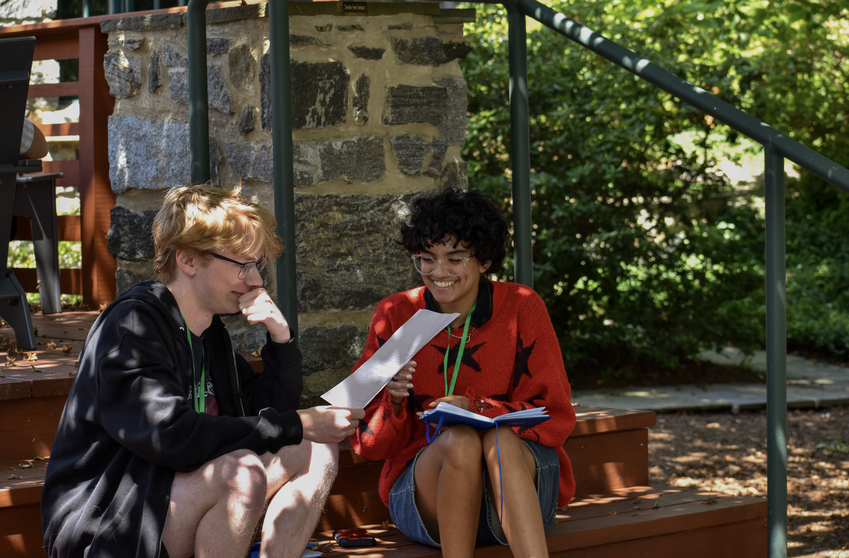 two people seated together smiling and looking at a paper