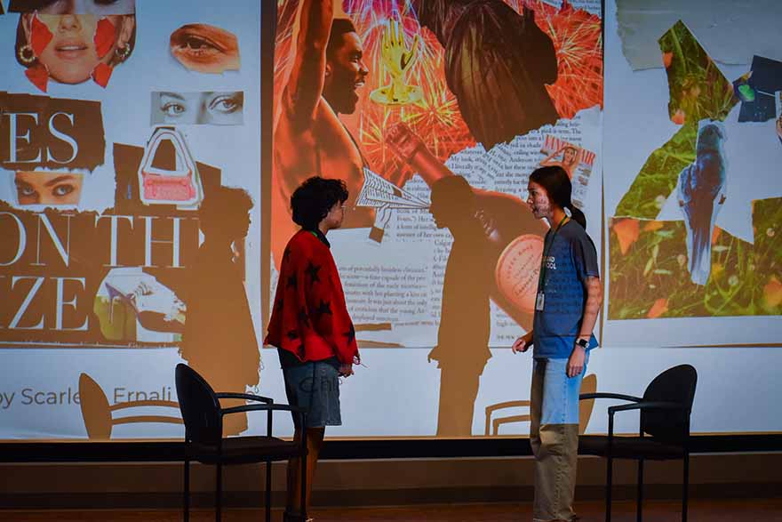 two people facing each other on stage in front of projected images and text